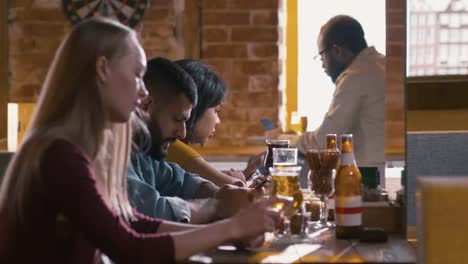 Young-people-sitting-at-bar-counter-with-cellphones