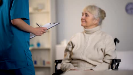 Therapist-making-notes-in-medical-records-and-examining-elderly-lady,-hospital