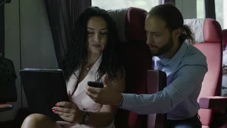 Business-coworkers-man-commuter-and-woman-working-and-consulting-together-about-office-project-on-modern-technology-tablet-pc-during-business-travel-by-train