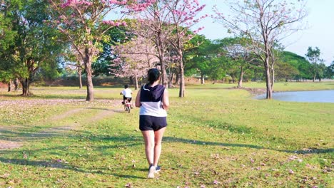 An-Asian-woman-jogging-in-natural-sunlight-in-the-evening,-along-with-his-son-riding-a-bicycle.--exercising-for-good-health.-Slow-Motion