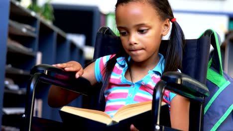 Vista-frontal-de-la-colegiala-afroamericana-discapacitada-leyendo-un-libro-en-la-biblioteca-en-la-escuela-4k