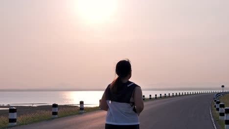 Übergewichtige-asiatische-Frauen-joggen-am-frühen-Morgen-im-Sonnenlicht-auf-der-Straße.-Konzept-des-Gewichtsverlustes-mit-Bewegung-für-die-Gesundheit.-Blick-nach-dem-Blick