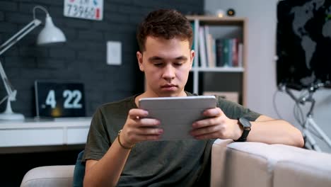 Close-up-portrait-of-a-teenager-playing-on-his-tablet-at-home,-looks-at-the-camera-at-the-end