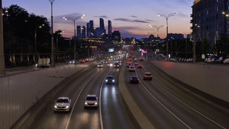 cars-drive-along-road-against-huge-modern-city-buildings