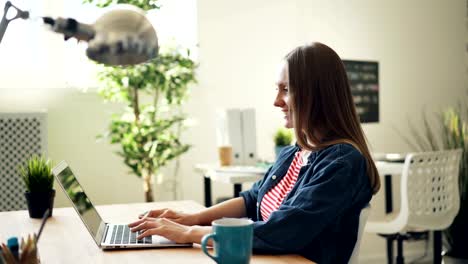 Side-view-of-pretty-girl-working-with-laptop-smiling-looking-at-screen-in-office