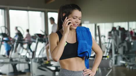 A-beautiful-young-woman-smiles-while-read-a-message,call-her-friends,-using-a-social-network-and-listen-to-the-music-at-the-gym.