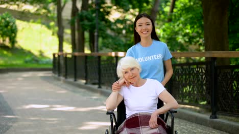 Sonriente-mujer-voluntaria-y-mujer-senior-discapacitada-buscando-cámara,-caridad