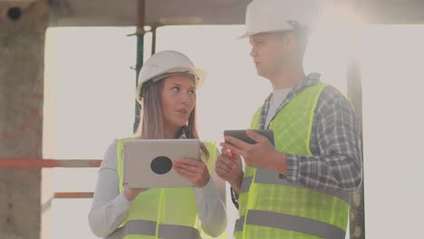 Engineers-designers-stand-on-the-roof-of-the-building-under-construction-and-discuss-the-plan-and-the-progress-of-construction-using-a-tablet-and-mobile-phone