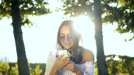 Junge-Frau-draußen-im-Park-lächelnd-und-SMS-auf-dem-Smartphone