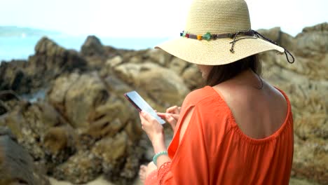 joven-hermosa-mujer-usando-el-teléfono-para-comunicarse-en-las-redes-sociales-y-sentarse-en-una-piedra-cerca-del-mar