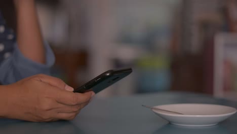 Woman-using-smart-phone-on-the-desk-and-drinking-a-cup-of-coffee-at-home.