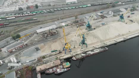 A-pile-of-sand-and-cargo-working-cranes-with-excavators-moving-river-sand-in-docks.-Industrial-part-of-city-with-cargo-trucks-and-tractors-working