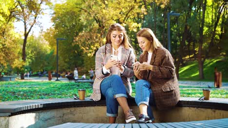 Amigos-alegres-usando-teléfonos-inteligentes-afuera-en-el-parque-público