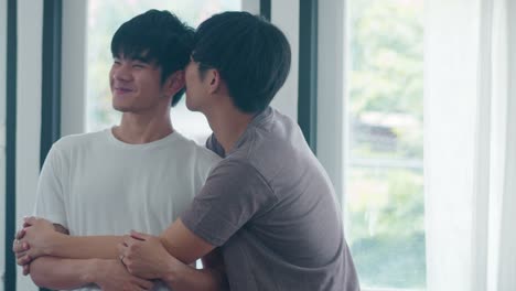 Asian-Gay-couple-standing-and-hugging-near-the-window-at-home.-Young-Asian-LGBTQ+-men-kissing-happy-relax-rest-together-spend-romantic-time-in-living-room-at-modern-house-in-the-morning-concept.