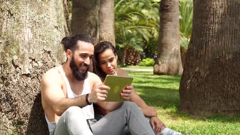 Hombre-y-mujer-relajándose-con-tableta-digital-en-el-parque-después-del-entrenamiento-deportivo