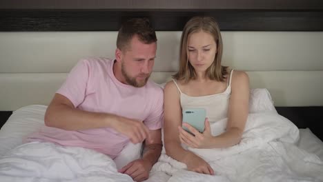 Junges-Paar-surft-internet-auf-dem-Handy-liegend-im-Bett