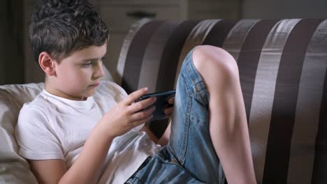 Teenager-boy-lies-on-a-sofa-and-uses-his-phone-for-games.-Social-media-and-child.-Cellphone-and-device-technology.-Phone-and-childhood.-Kid-and-telephone-in-life.-Cell-and-gadget.