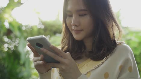 Close-up-shot-of-4K-footage-of-young-asian-woman-using-mobile-to-sending-a-massage-to-her-friends-at-sunset.