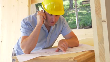 CLOSE-UP:-Junger-Bauleiter-diskutiert-Grundrisse-am-Telefon.