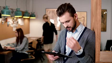 young-handsome-bearded-man-uses-touchscreen-tablet-in-the-modern-startup-office