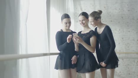 Three-Young-and-Beautiful-Ballerinas-Use-Smartphone.-Shot-on-a-Bright-and-Sunny-Day-in-Light-and-Modern-Studio.