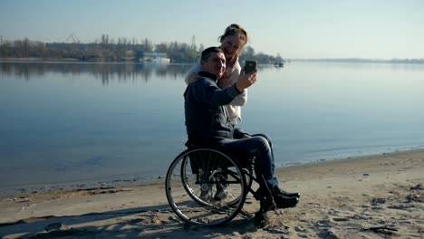 Disabled-man-and-girl-takes-pictures-(selfie),-smiling-man-and-woman-near-river