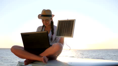 chica-en-vacaciones-se-sienta-en-el-coche-de-la-azotea-con-laptop-de-cargos-módulo-solar-en-contraluz,-mujer-sentada-en-coches-de-época-con-la-computadora