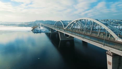 Auto-und-Zug-bewegt-sich-auf-einer-Brücke-über-einen-gefrorenen-Fluss-Luftbild-Drohne-Filmmaterial