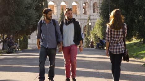 Young-lovely-gay-couple-tourists-walk-in-park-road-with-trees-colosseum-in-background-in-rome-at-sunset-holding-hands.-Boyfriend-gets-jealous-when-beautiful-girl-walks-by-glancing.-Slow-motion