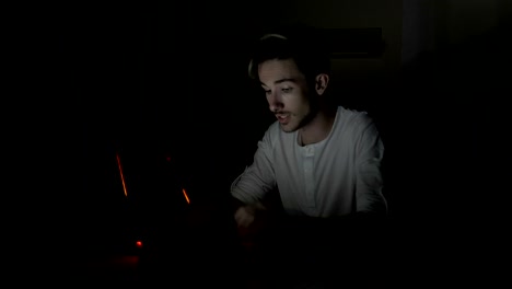 Young-attractive-student-male-video-chatting-and-waving-at-web-camera-in-a-dark-room-at-home