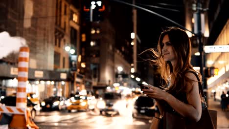 Young-beautiful-woman-standing-in-the-evening-in-traffic-downtown-and-using-the-smartphone-in-New-York,-America