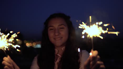 Eine-junge-Frau-mit-langen-dunklen-Haaren-hält-Feuerwerk-in-der-Nacht-im-Hintergrund-der-Stadt-und-ist-glücklich,-guten-Laune-zu-haben.-Slow-Motion.-Porträt.-4K