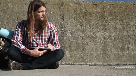 Backpacker-de-turística-de-hombre-sentado-con-la-tablet-en-la-pared-al-aire-libre-4K