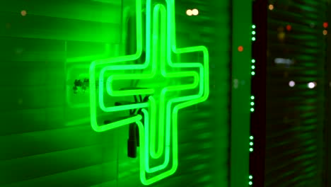 panning-of-marijuana-dispensary-neon-green-weed-cross-on-city-store-front-window