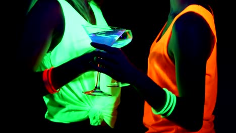 Women-with-UV-face-paint,-glowing-bracelets,-drinks,-glowing-clothing-dancing-together-in-front-of-camera,-Close-up-of-drinks.-Caucasian-and-asian-woman.-.