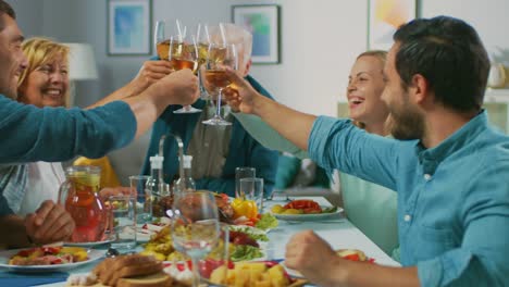 Große-Familie-und-Freunde-feiern-zu-Hause,-vielfältige-Gruppe-von-Menschen-versammelten-sich-am-Tisch-anstoßen-in-einem-Toast.-Leute-Essen,-trinken-und-Spaß-haben.-Tagsüber-Festlichkeit-im-Wohnzimmer.