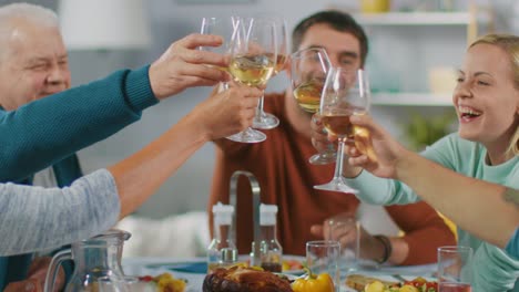 Familia-y-fiesta-de-amigos-en-casa,-grupo-diverso-de-niños,-jóvenes-y-viejas-personas-se-reunieron-en-la-mesa-tienen-divertida-conversación.-Tintineo-de-vasos-y-haciendo-tostadas.-En-cámara-lenta.