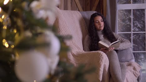 A-girl-sits-in-a-chair-near-the-Christmas-tree-and-reads-a-book.