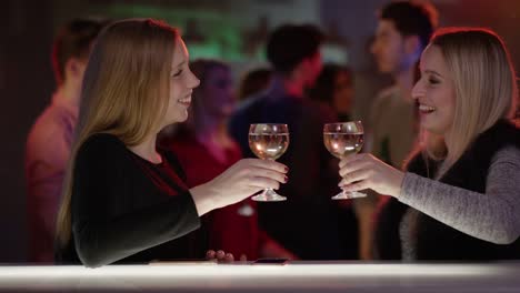 two-attractive-girls-at-bar-in-club-talking-and-raising-their-glasses