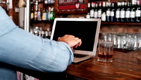 Man-using-laptop-while-having-whisky-at-counter