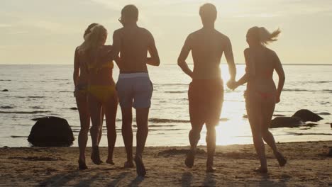 Gruppe-junger-Menschen,-die-in-Sunset-Light-ins-Wasser-laufen.-Slow-motion-60-FPS.