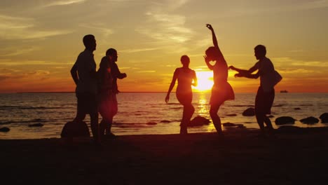 Grupo-de-jóvenes-felices-están-bailando-en-la-playa-en-Sunset-Light