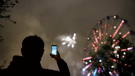 Closeup-de-silueta-de-hombre-viendo-y-fotografiando-fuegos-artificiales-explotan-sobre-smartphone-cámara-al-aire-libre