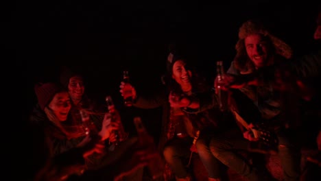 Young-friends-making-a-toast-with-beer-around-campfire