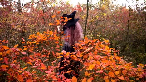 Young-pink-hair-witch-behind-the-yellow-bush-in-the-mystical-autumn-forest.-Halloween-preparation.