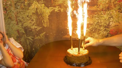 Fast-motion.-Girl-clapping-by-hands.-Sitting-girl-afraid-of-fire.-Sparkling-fire-fountains-in-a-cake.-Girls-Birthday.-Cake-with-lights.-Girl-is-sitting-looking-at-the-cake-and-afraid.