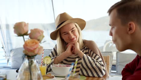 Joven-pareja-hablar-desayunando-en-el-yate.-Gente-hermosa-con-paisaje-marino-en-el-fondo.