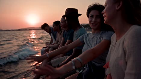 Young-multi-ethnic-hipster-friends-on-summer-holidays-sitting-on-jetty