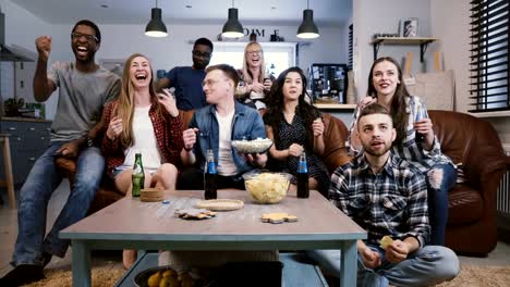 Freunde-Sportübertragungen-im-Fernsehen,-jubeln-und-feiern.-Glücklich-diverse-Fans-Fans-sitzen-auf-der-Couch-mit-Popcorn-und-Getränken.-4K