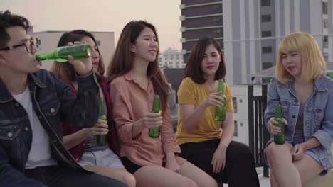 Group-of-young-asian-women-and-man-people-dancing-and-raising-their-arms-up-in-air-to-the-music-played-by-dj-at-sunset-urban-party-on-rooftop.-Young-asian-girls-and-boy-friends-hanging-out-with-drinks